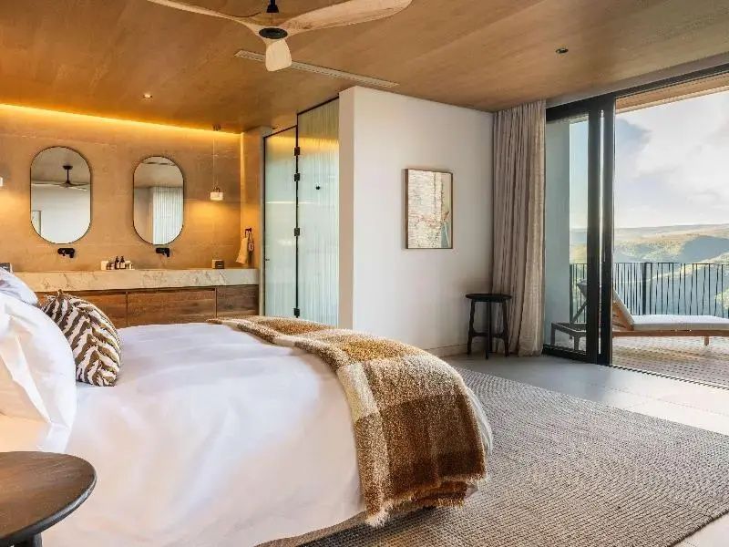 Modernes Schlafzimmer mit Doppelbett, Holzdecke, Deckenventilator und Blick zum Balkon.
