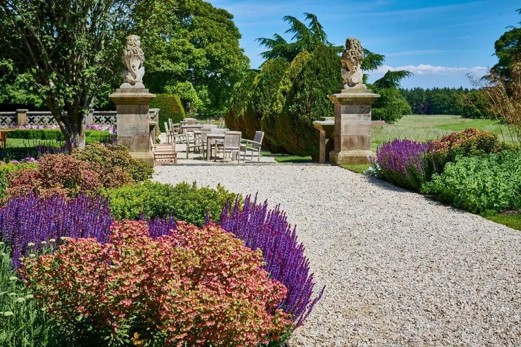 Kiesweg im gepflegten Garten mit historischen Steinsäulen und Tischen im Freien.