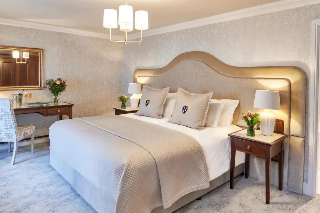Großes Doppelbett mit beigen Kissen und verziertem Kopfteil in einem hellen Zimmer.