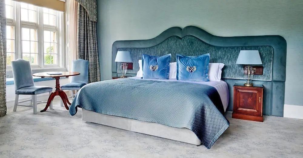 Doppelbett mit blauer Steppdecke, samtenem Kopfteil und zwei bestickten Kissen.