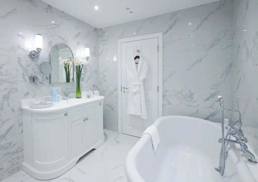 Hell gefliestes Badezimmer mit marmorierten Wänden, freistehender Badewanne und Waschbecken.