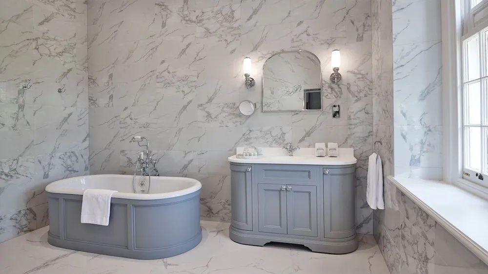 Marmoriertes Badezimmer mit grauer Waschkommode, Wandleuchten und freistehender Wanne.