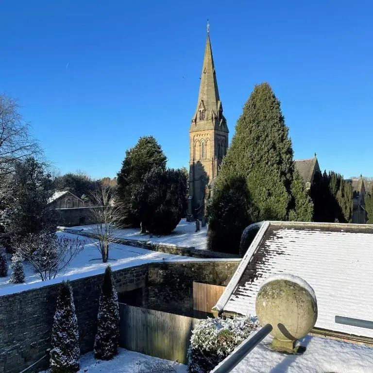 Verschneiter Garten und Kirchturm unter blauem Himmel im Winter, von oben fotografiert.