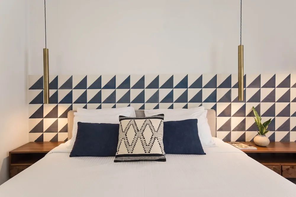 Doppelbett mit dekorativen Kissen vor einer blau-weiß gemusterten Wand im Hotelzimmer.