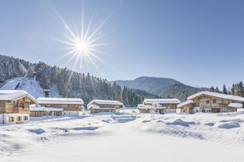 Verschneite Chalets des Relais & Châteaux Gut Steinbach Hotels in winterlicher Bergkulisse unter strahlender Sonne, eingebettet in eine idyllische Alpenlandschaft mit klarem, blauem Himmel.