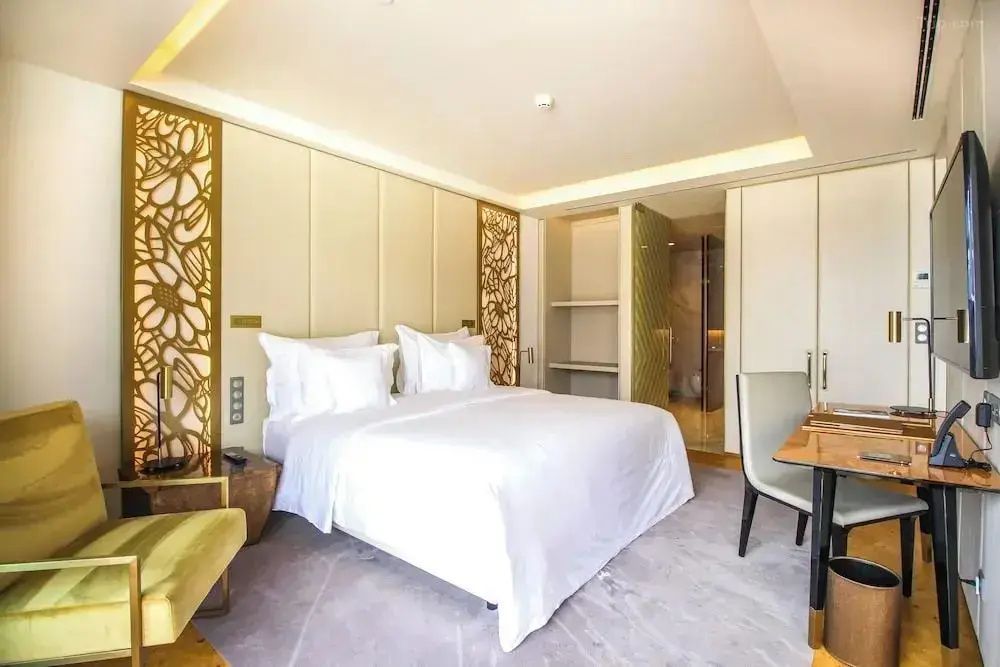 Helles Hotelzimmer mit Doppelbett, weißer Bettwäsche, Schreibtisch und Wanddekor in Goldtönen.