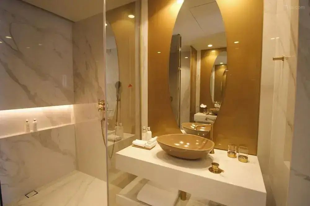Badezimmer mit weißem Waschtisch, goldenem Spiegelelement und verglaster Dusche.