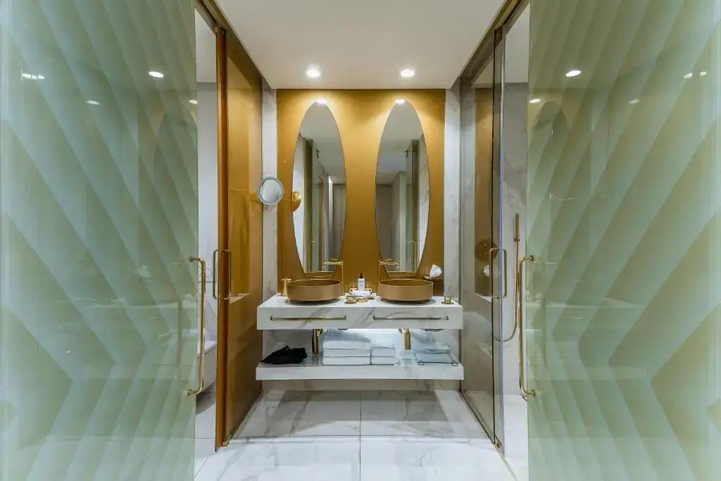 Badezimmer mit doppeltem Waschtisch, zwei goldenen Waschbecken und zwei ovalen Spiegeln.
