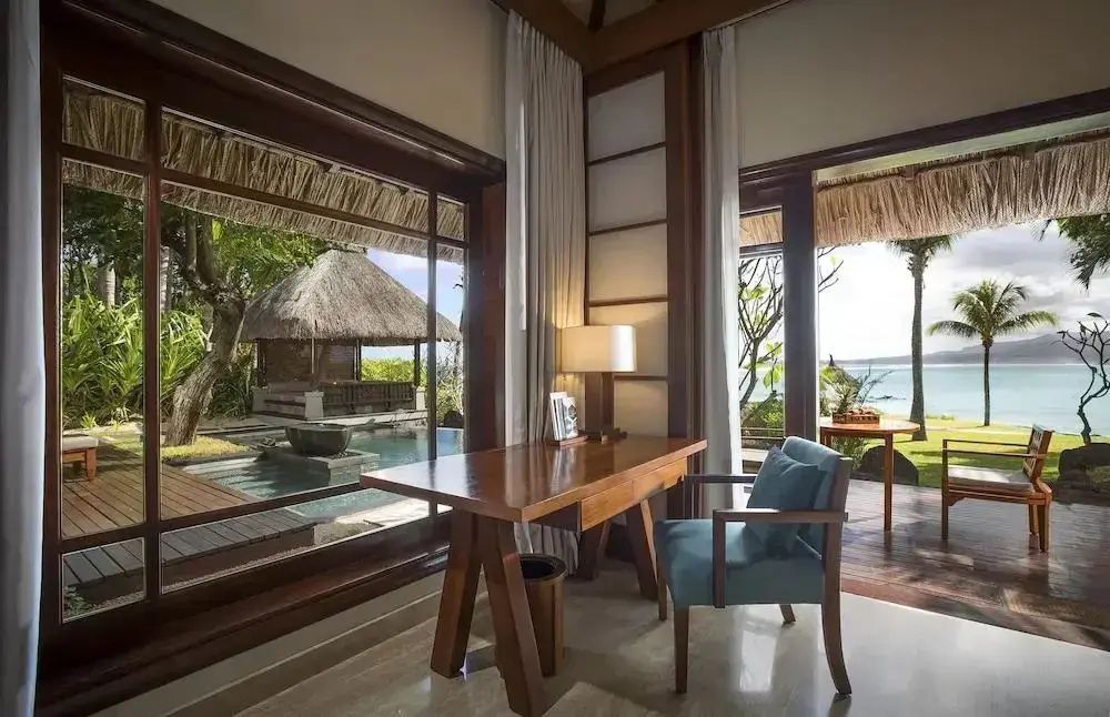 Holzschreibtisch im Zimmer mit Blick durch das Fenster auf Terrasse, Pool und das Meer.