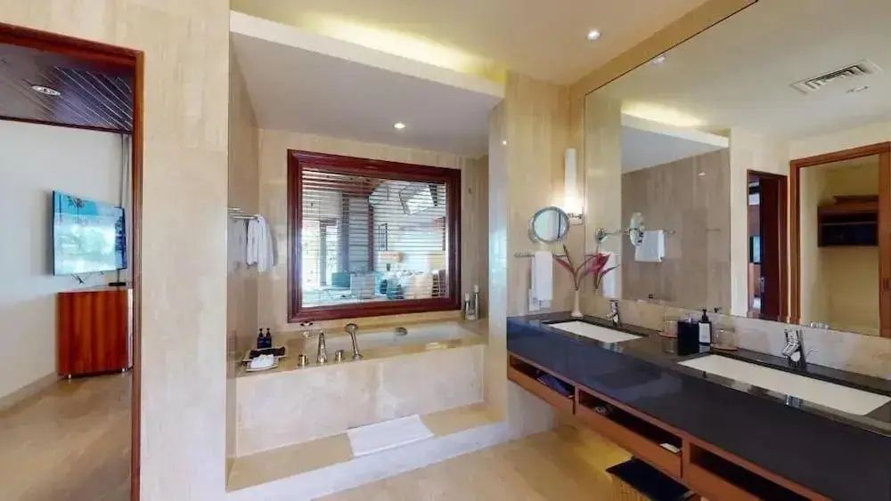 Badezimmer mit einer tief eingelassenen Badewanne und einem Waschtisch unter einem Spiegel.