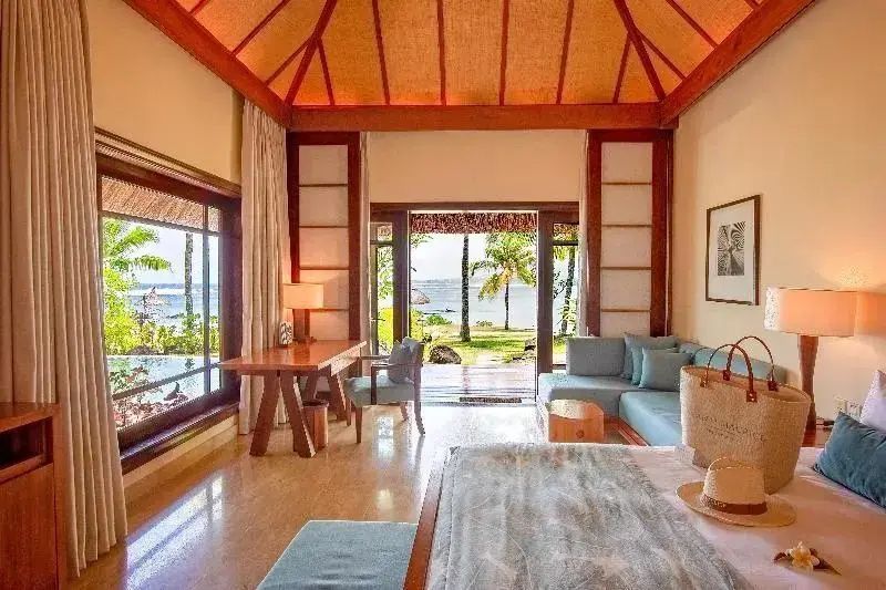Sonniges Hotelzimmer mit hohem Holzdach, Schreibtisch, Ecksofa und Blick ins Grüne und Meer.