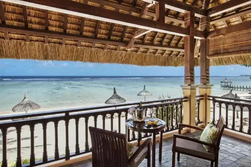 Überdachter Balkon mit Holzstühlen und direktem Blick auf den Strand und das Meer.