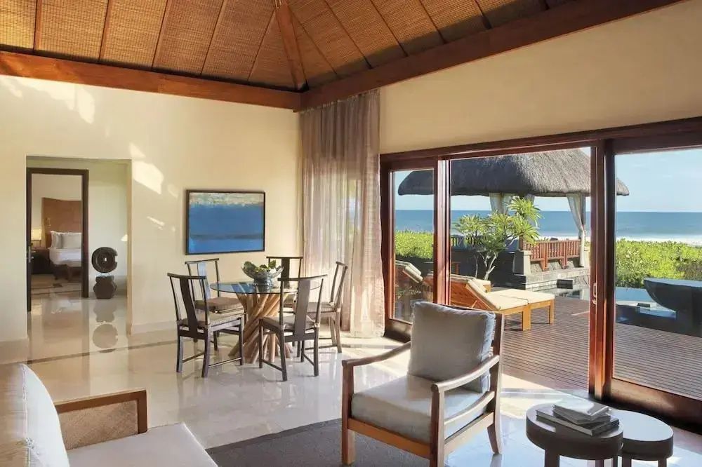 Wohnbereich mit Esstisch, Sesseln und großen Glasschiebetüren mit Blick auf Meer und Terrasse.