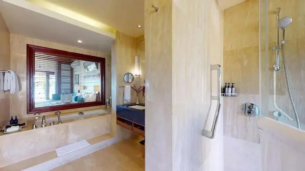 Badezimmer in Naturtönen mit eingelassener Badewanne, Waschtisch und großem Spiegel.