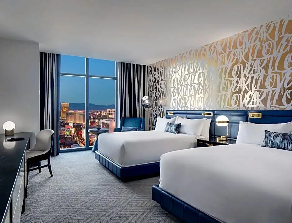 Doppelzimmer mit zwei großen Betten, blauen Kopfteilen und Blick auf die Stadt.