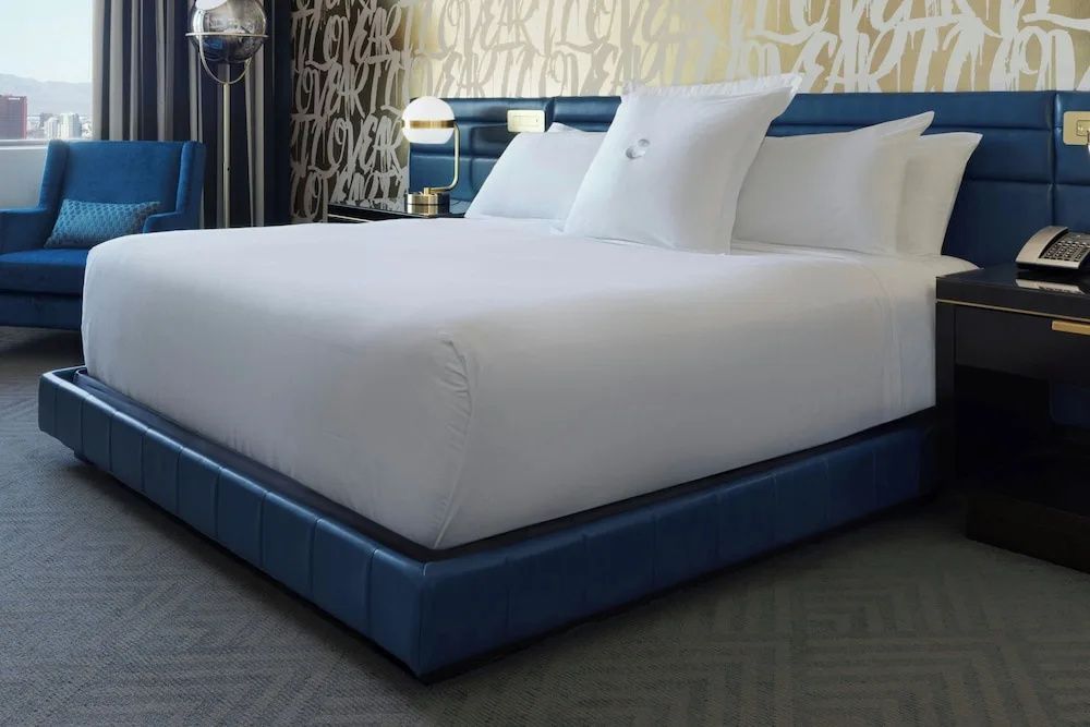 Großes Doppelbett mit weißer Bettwäsche und blauem Bettrahmen im Hotelzimmer.