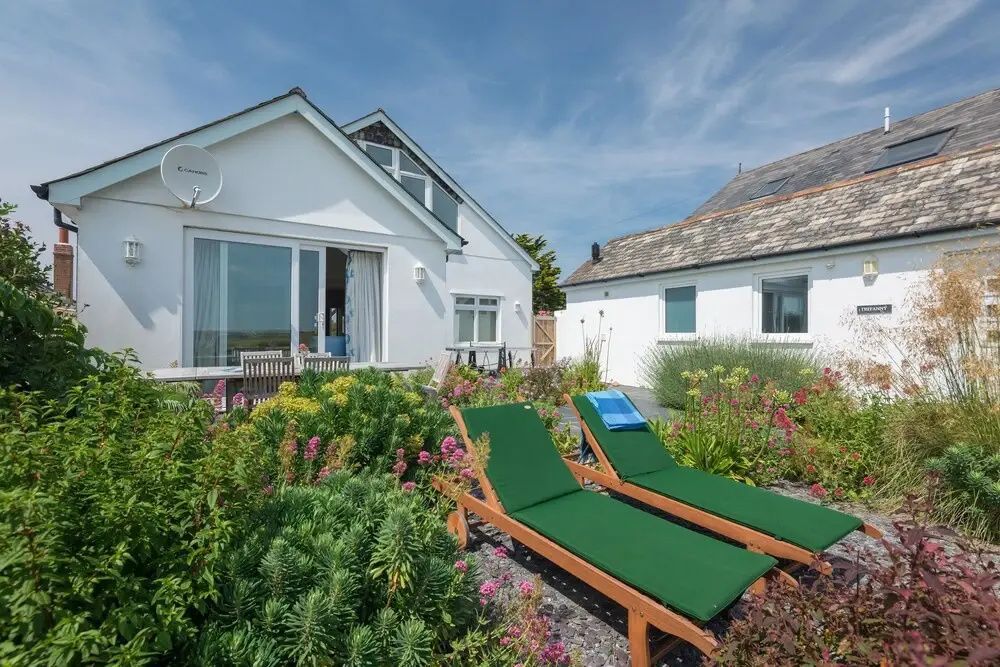Weißes Ferienhaus mit Terrasse und Garten sowie zwei Sonnenliegen im Vordergrund.
