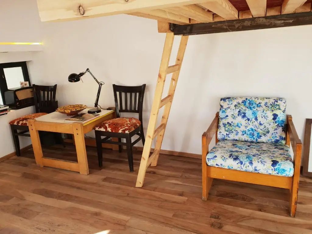 Ein Zimmer mit Holzboden, Sessel, Schreibtisch und Holzleiter zum Schlafbereich.
