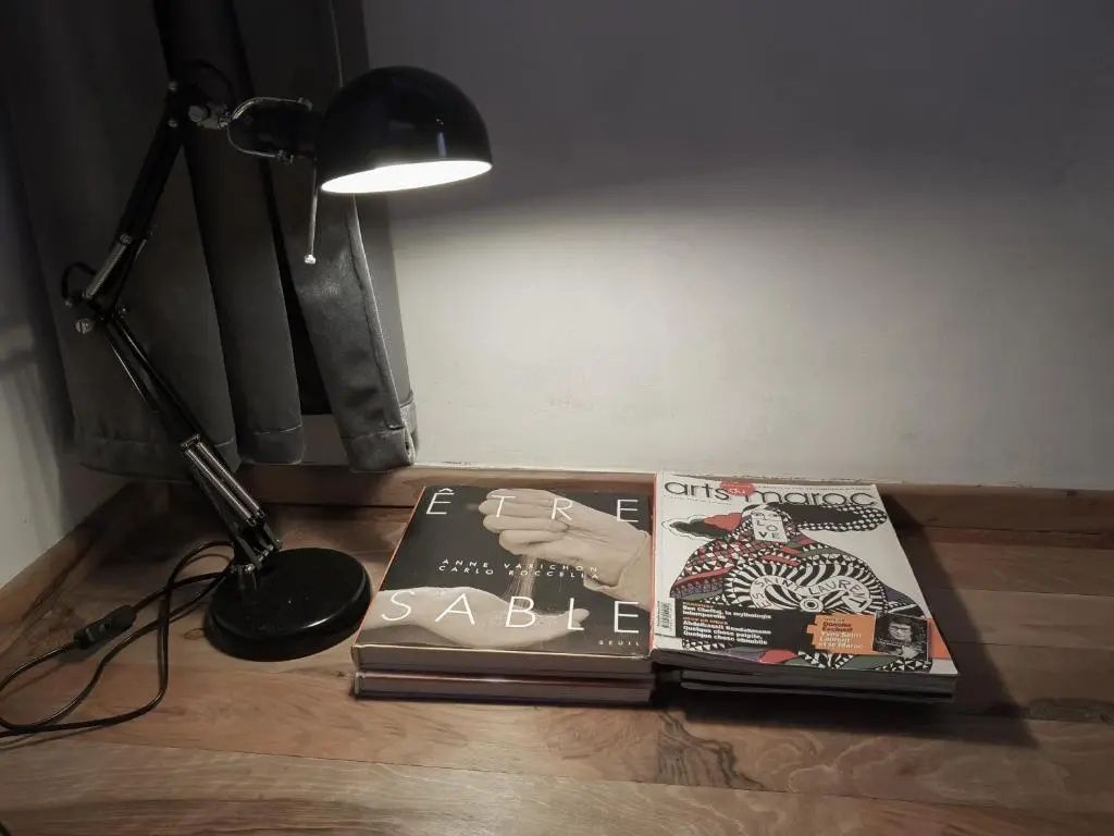 Schwarze Tischleuchte leuchtet auf aufgestapelte Kunstbücher auf Holztisch.