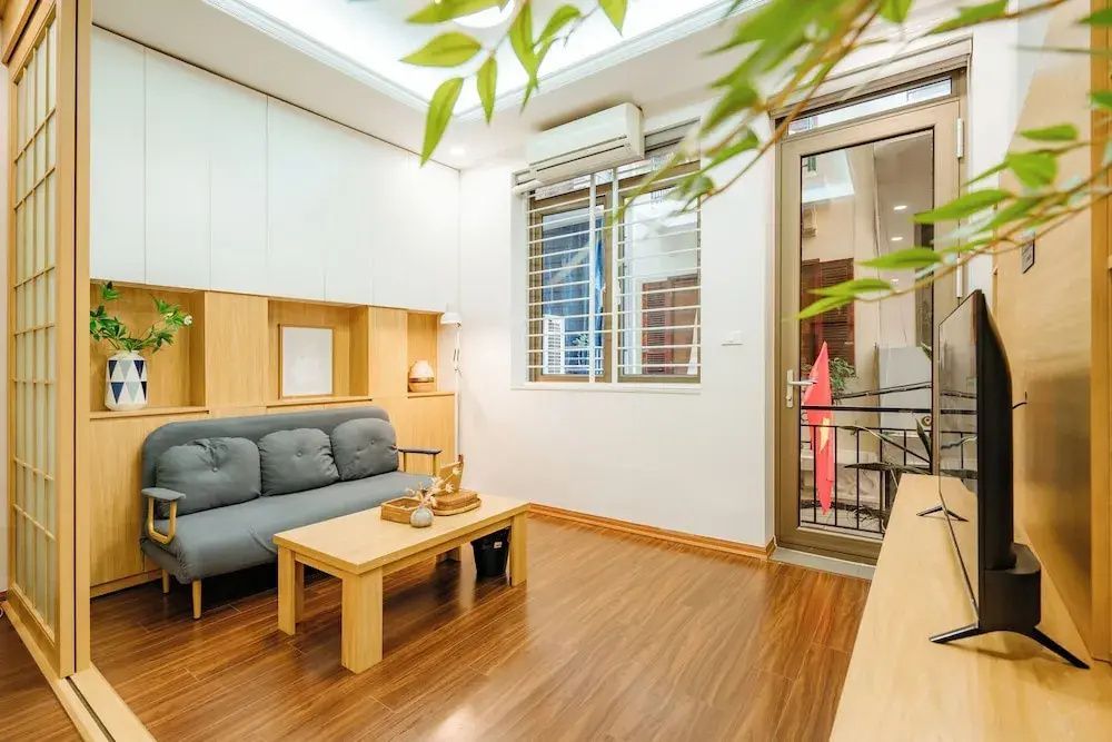 Wohnbereich mit einem grauen Sofa, Holztisch, Parkettboden und Tür zum Balkon.