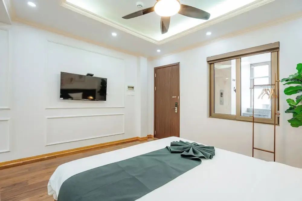 Modernes Schlafzimmer mit weißem Bett, flachem Fernseher an der Wand und Deckenventilator.