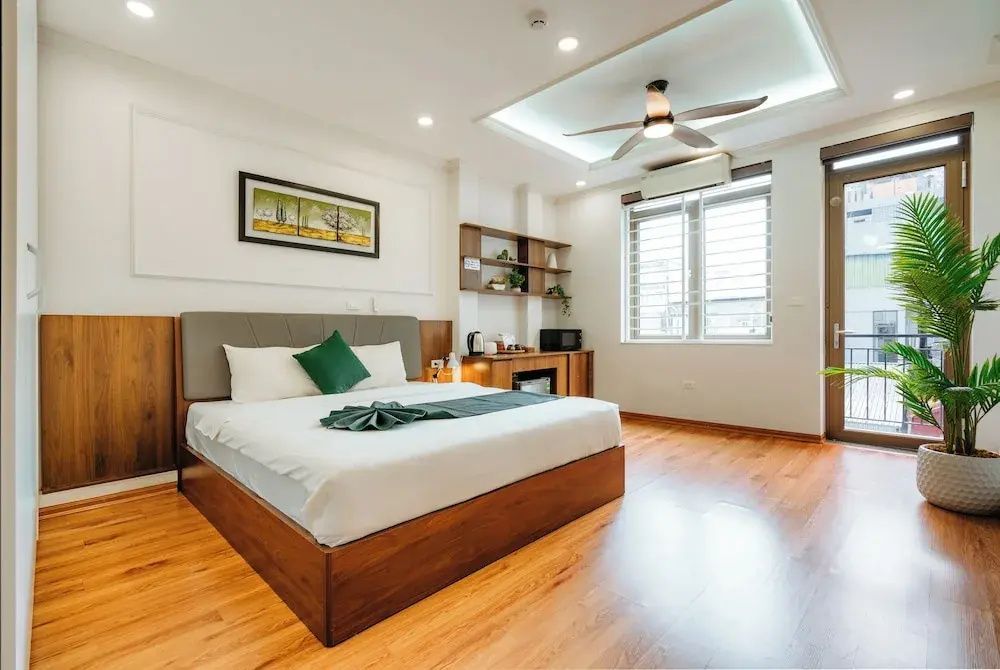 Helles Hotelzimmer mit Doppelbett, Parkettboden, Holzschreibtisch und einem Deckenventilator.