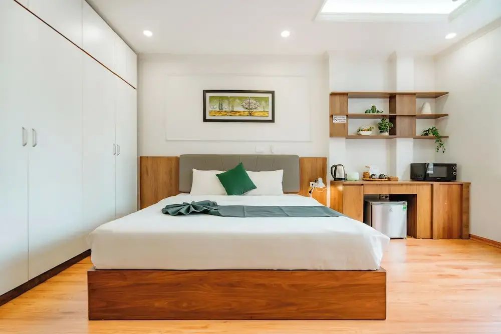 Doppelbett mit weißer Bettwäsche, grünem Kissen, weißem Kleiderschrank und Holzschreibtisch.