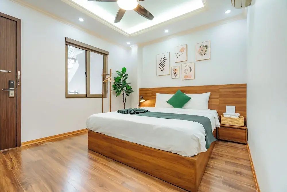 Helles Schlafzimmer mit Doppelbett aus Holz, Wandbildern und einer Pflanze im Raum.