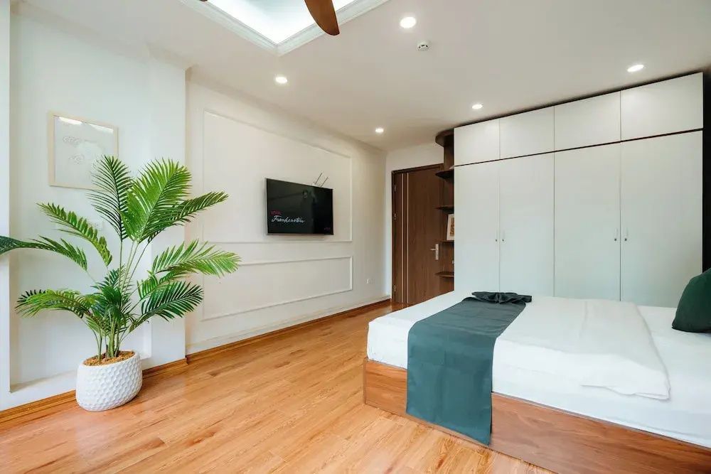 Hotelzimmer mit Flachbildfernseher an der Wand, Zimmerpflanze und Einbauschrank.