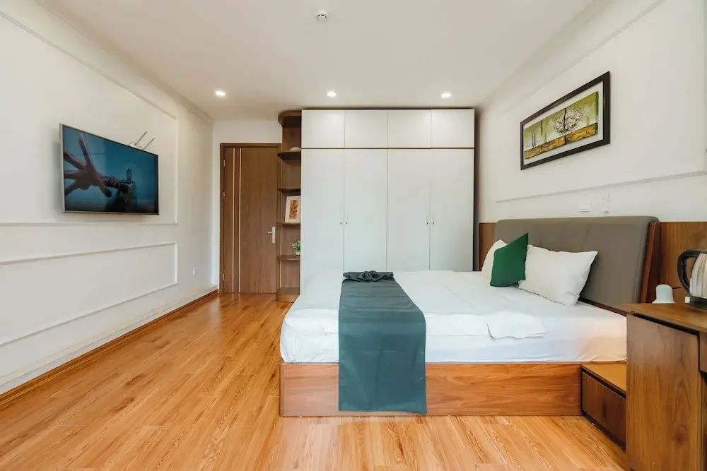 Helles Hotelzimmer mit Doppelbett, Parkettboden, modernem Kleiderschrank und Wandfernseher.