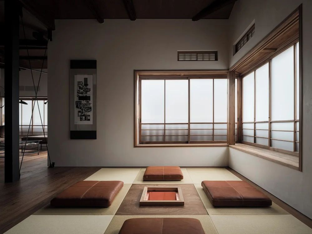 Japanischer Tatami-Raum mit Sitzkissen am niedrigen Tisch, Wandbild und Shoji-Schiebetüren.