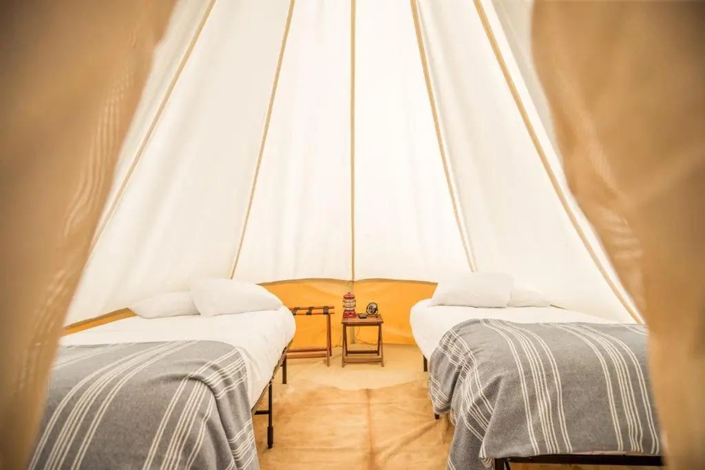 Innenansicht von einem Glampingzelt mit zwei Einzelbetten und Holzmöbeln.