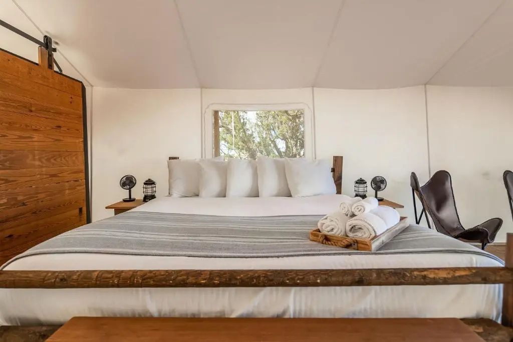 Doppelbett mit Kissen und angerichteten Handtüchern im hellen Zelt mit Holzansatz.