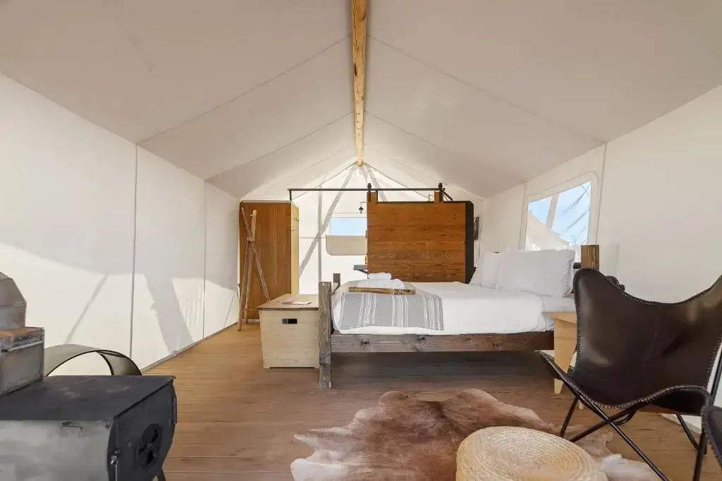 Innenraum eines Zeltes mit Holzboden, Kaminofen, Holzmöbeln und einem Doppelbett.