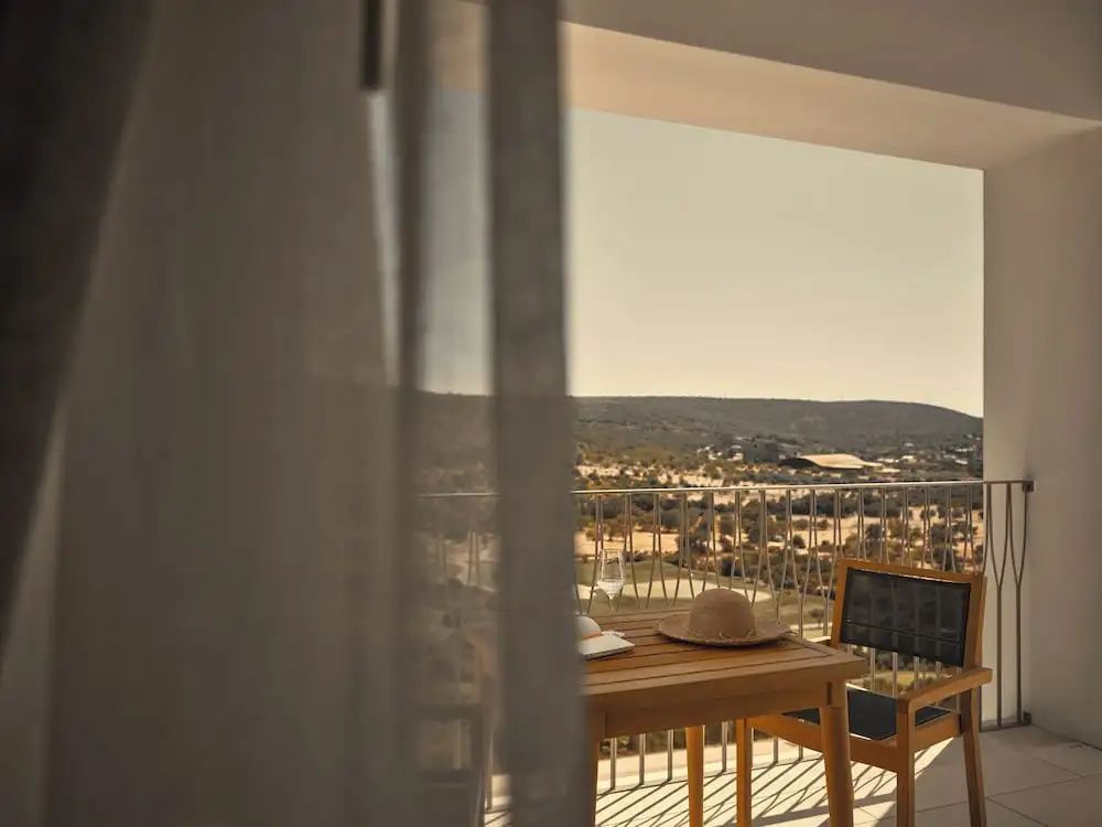 Blick vom Balkon mit Holzmöbeln auf die umliegende hügelige Landschaft der Algarve.