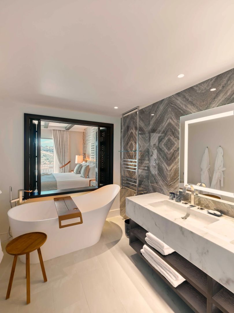 Badezimmer mit freistehender Badewanne, Marmorwaschtisch und Durchblick zum Schlafzimmer.