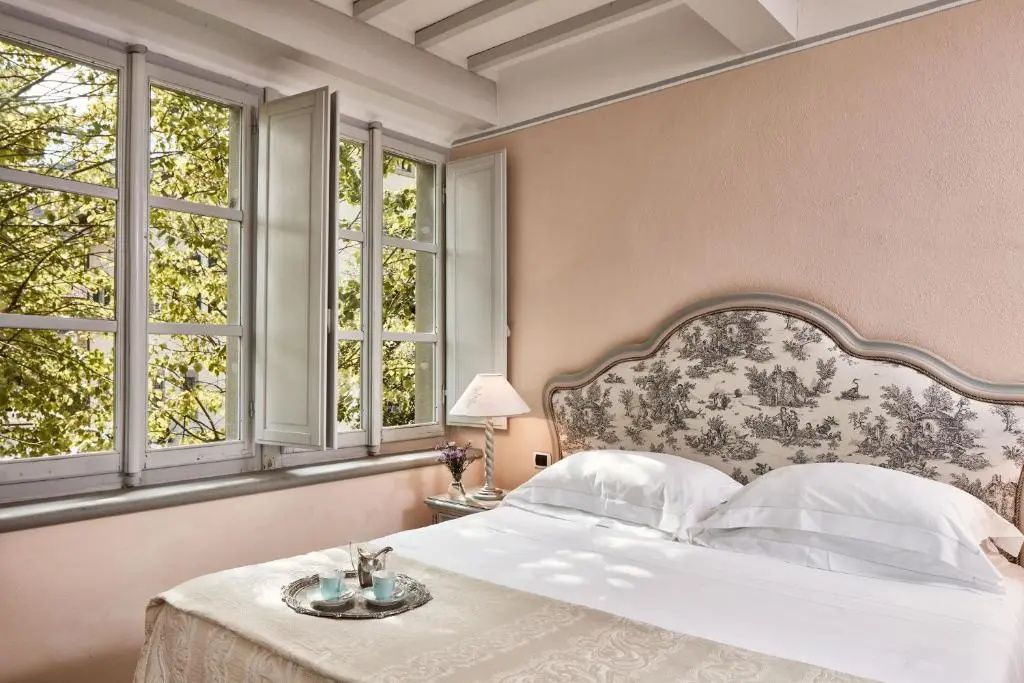 Doppelbett mit gemustertem Kopfteil und geöffnete Fenster mit Blick ins Grüne.