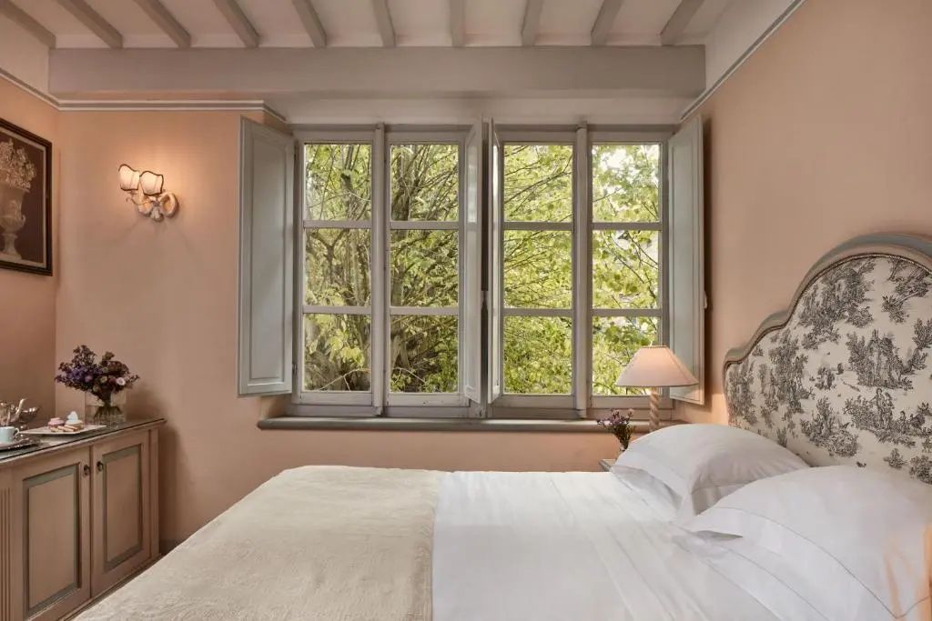 Helles Hotelzimmer mit großem Fenster, Blick auf grüne Bäume und Doppelbett.