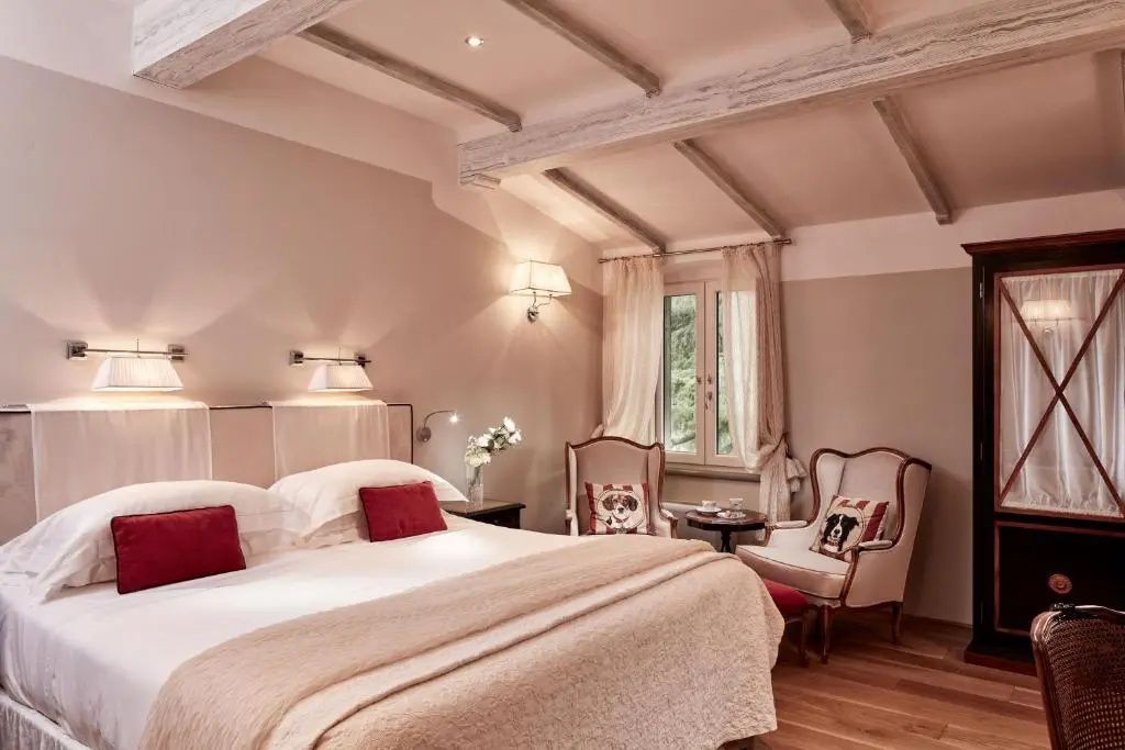 Helles Zimmer mit Dachschräge, großem Bett, roten Kissen und Sitzgelegenheit am Fenster.