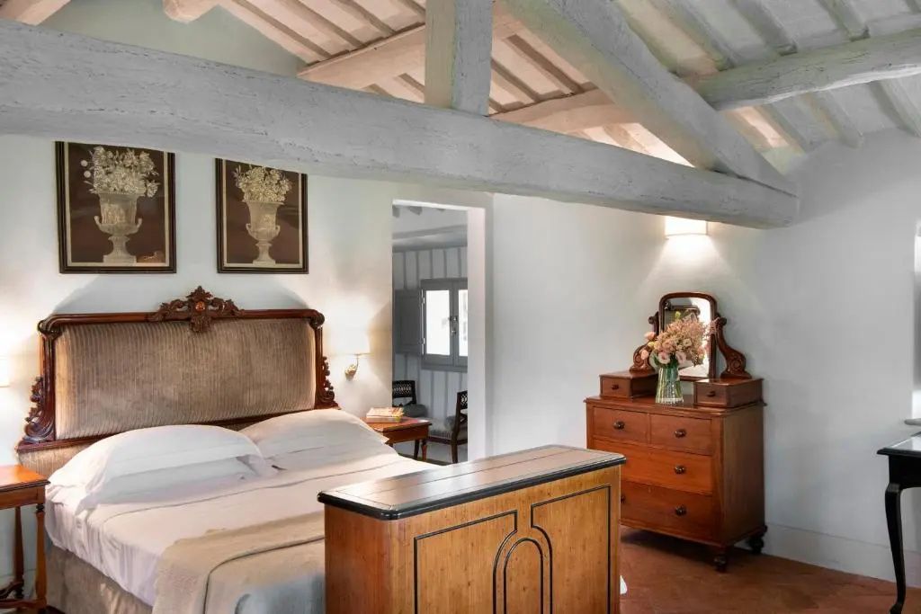 Rustikales Schlafzimmer mit weiß geweißten Holzbalken, Bett und antikem Kommodenschrank.