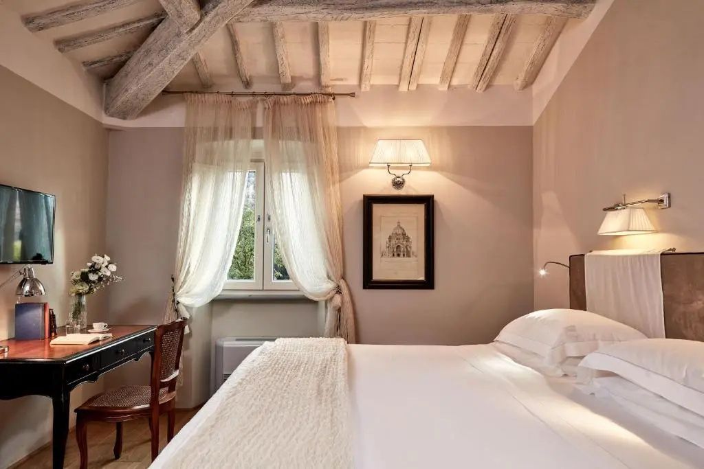 Schlafbereich mit Holzbalkendecke, weißem Bett, Schreibtisch und Fenster.