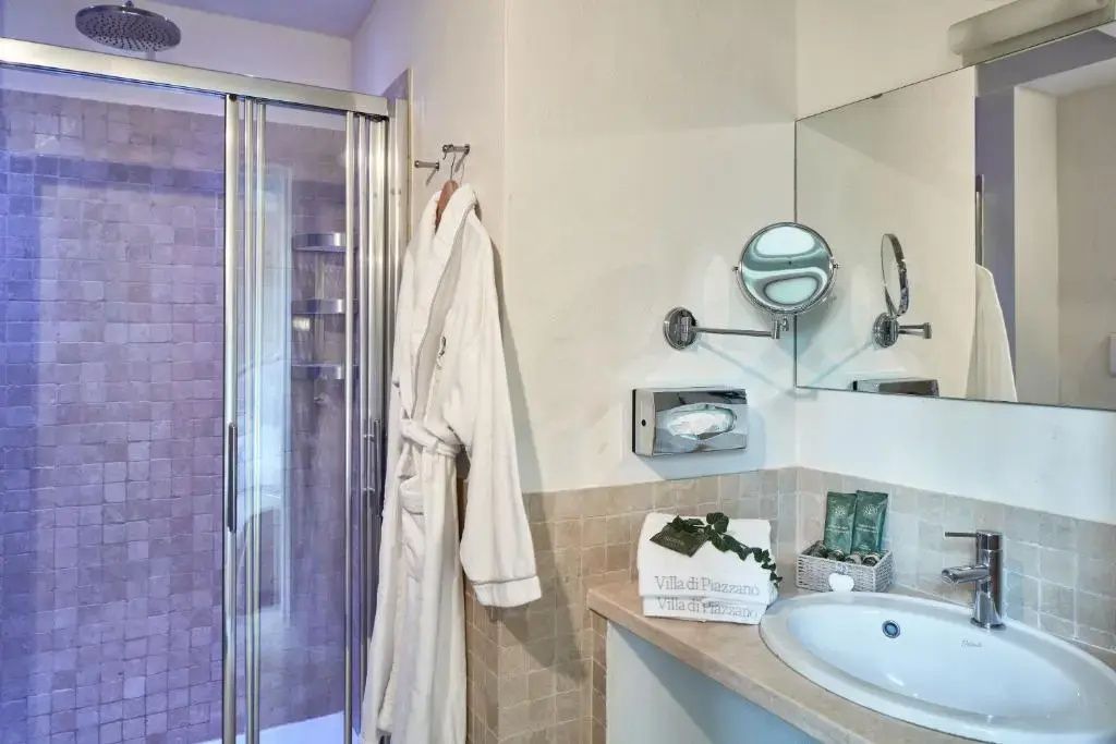 Badezimmer mit Glasduschkabine, Waschbecken und weißem Bademantel.