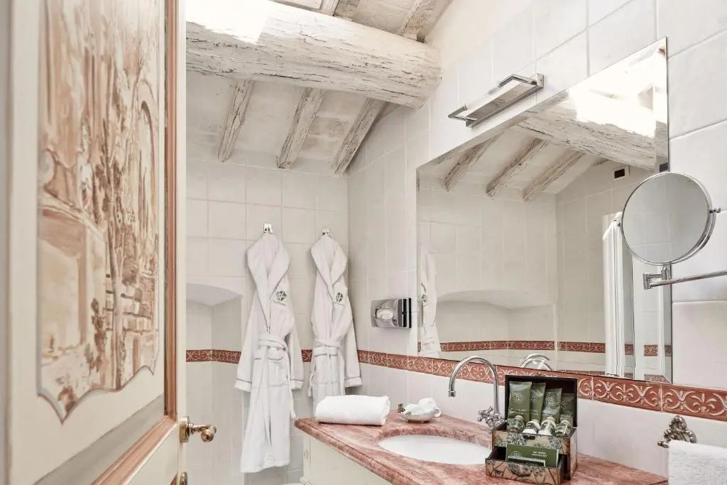 Badezimmer mit Marmorwaschtisch, großem Spiegel, Bademänteln und weißer Holzbalkendecke.