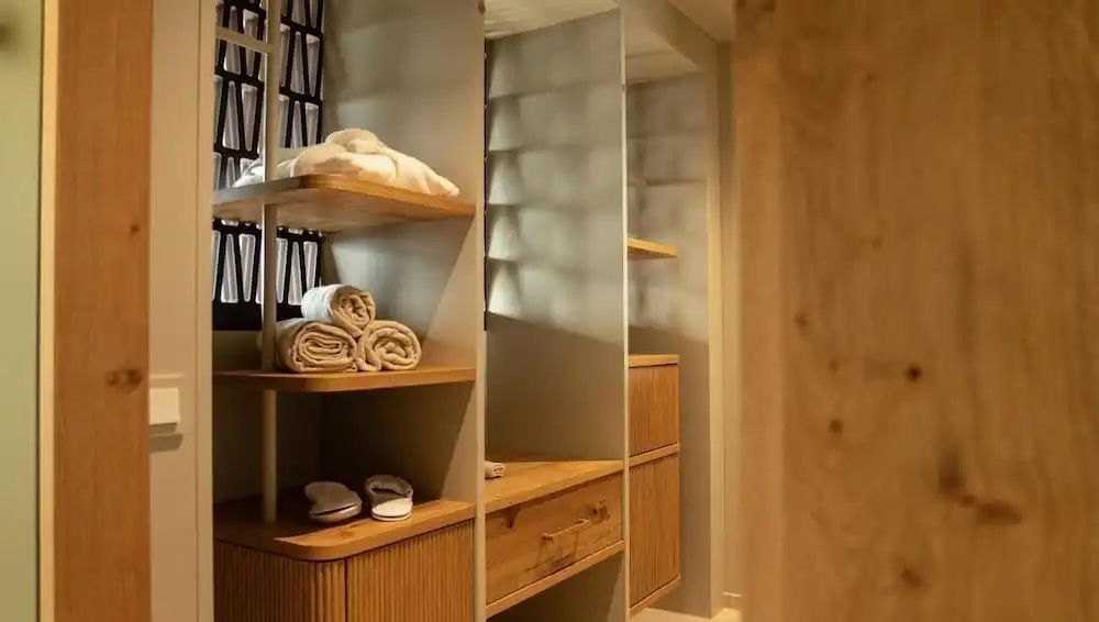 Offener Holzschrank im Zimmer mit zusammengelegten Handtüchern, Bademänteln und Hausschuhen.