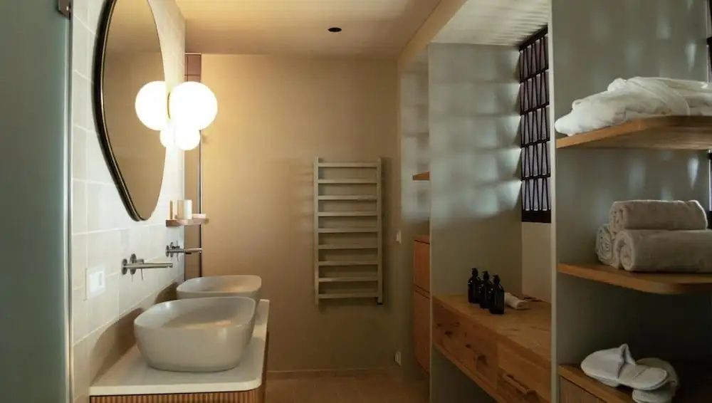 Badezimmer mit zwei Aufsatzwaschbecken, beleuchtetem Spiegel und einer Wandgarderobe.