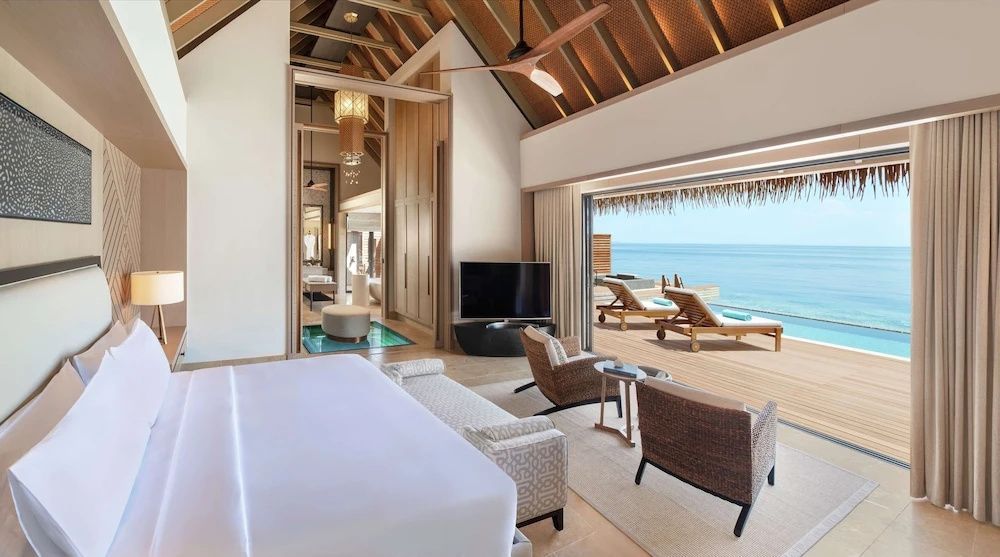Blick aus dem Schlafzimmer auf die Sonnenterrasse mit Liegen und das Meer.