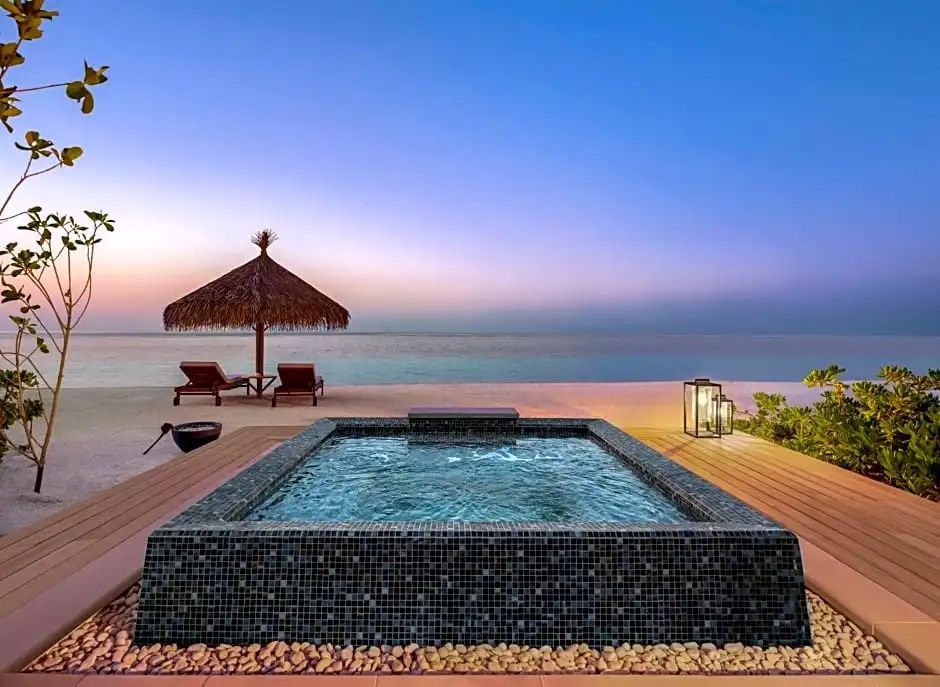 Privater Pool auf einer Holzterrasse mit Blick auf das Meer bei Dämmerung und zwei Sonnenliegen.