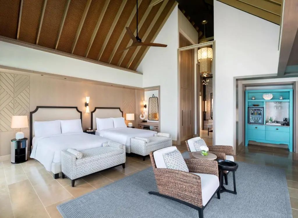 Hotelzimmer mit zwei großen Betten, Sitzgruppe und hohen Decken in Holzoptik.