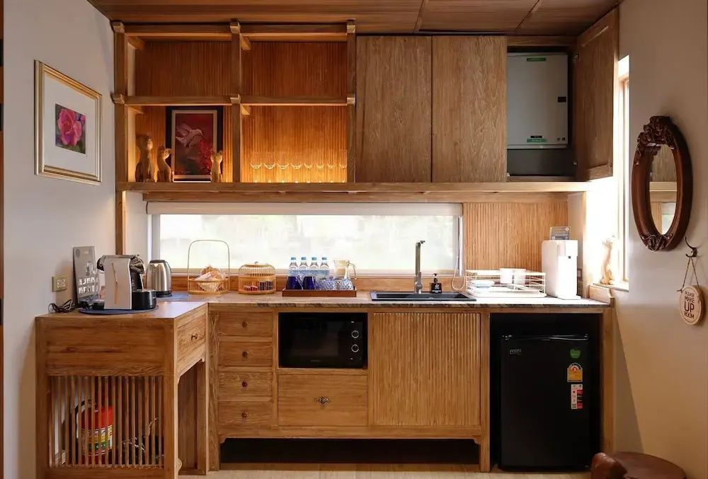 Kleine Küchenzeile aus Holz mit Mikrowelle, Spüle, Kühlschrank und Regalen.