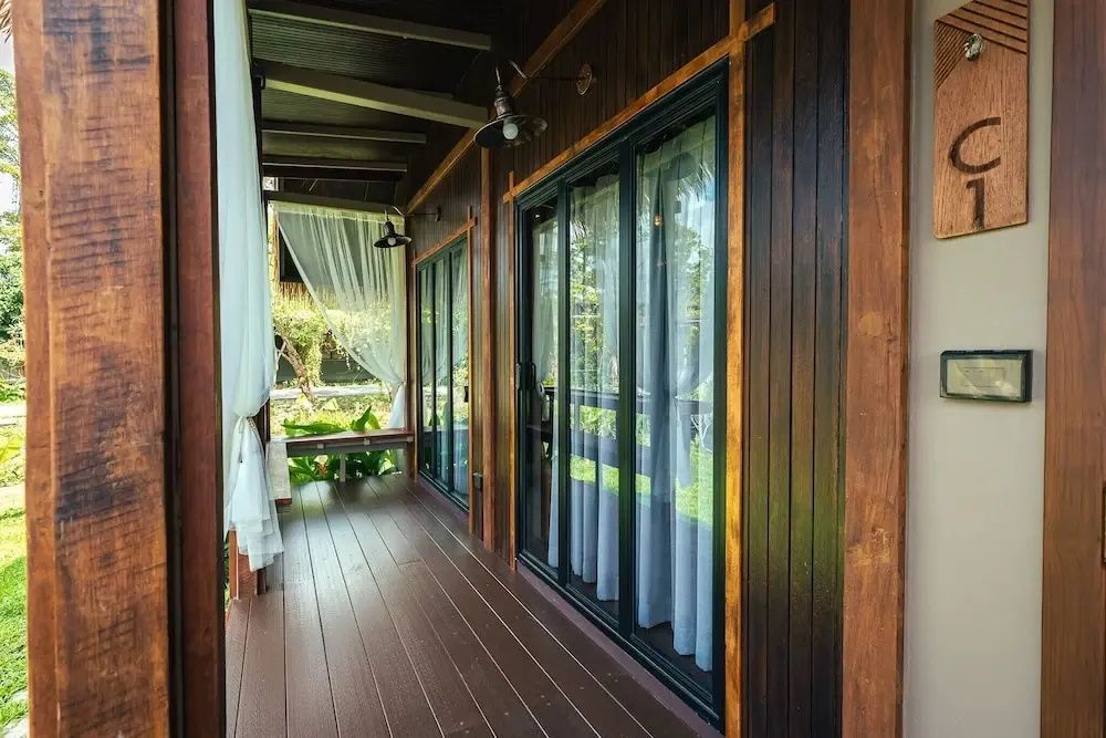 Überdachte Holzterrasse mit Schiebetüren aus Glas und weißen Vorhängen.